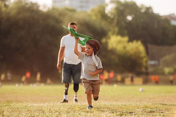 Running with toy plane, imagination. The amputee father is with his son on the field.