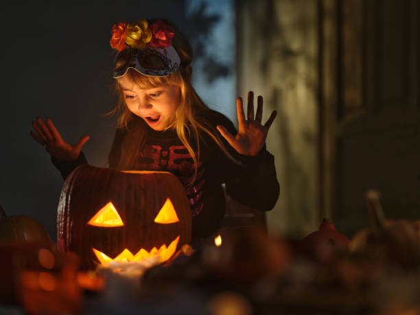 Shocked girl in a costume looking inside of Jack O' Lantern during Halloween at home.